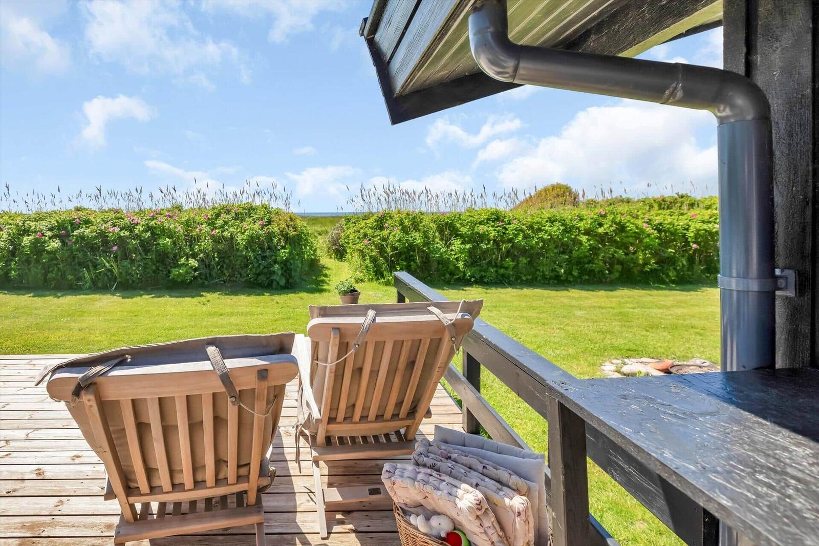 Zwei Holzstühle auf einer Terrasse mit Blick auf Gras und Hecke.