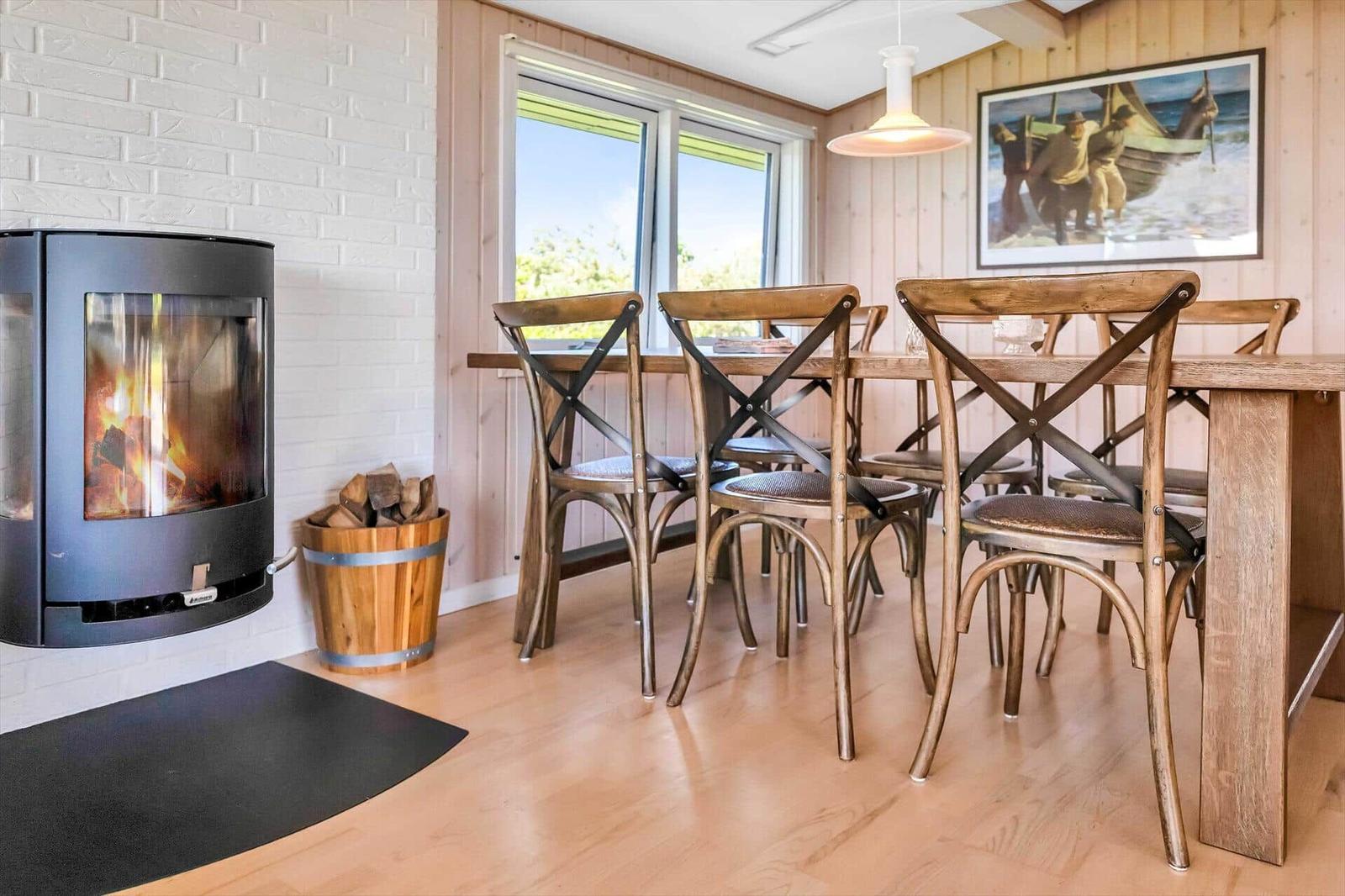 Esszimmer mit Holztisch, Stühlen und Kaminofen an weißer Wand.