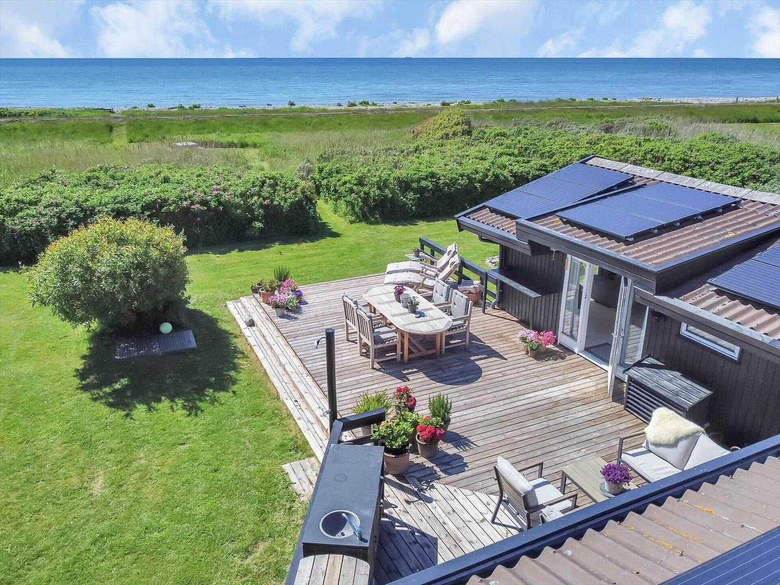 Terrasse mit Garten und Meerblick. Solaranlage auf Dach. Möbel und Pflanzen.