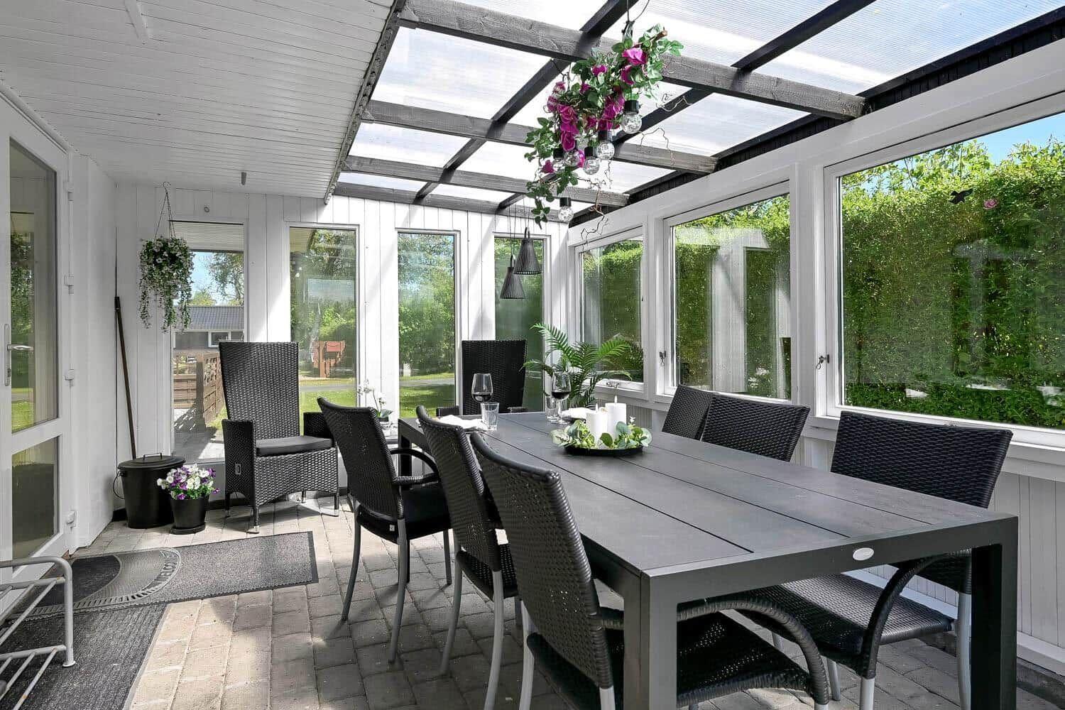 Terrassenbereich mit Tisch und Stühlen, Glasdach und Blick auf Grünflächen.
