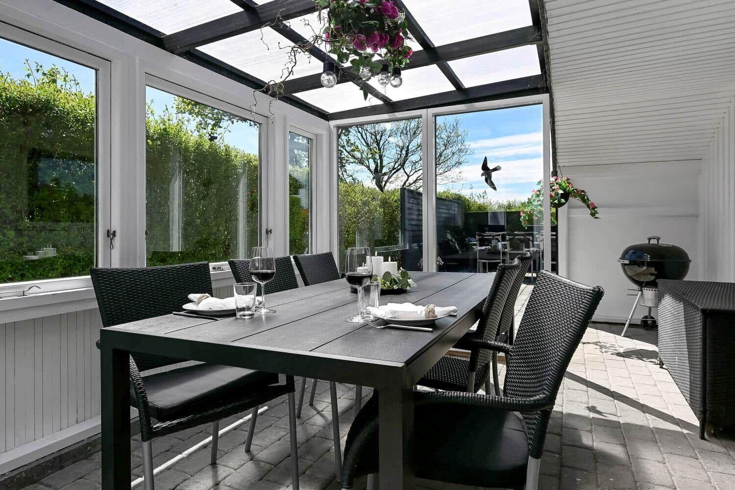 Gartenbereich mit Tisch, Stühlen und Grill. Durchgehende Glaswände und Pflanzen.