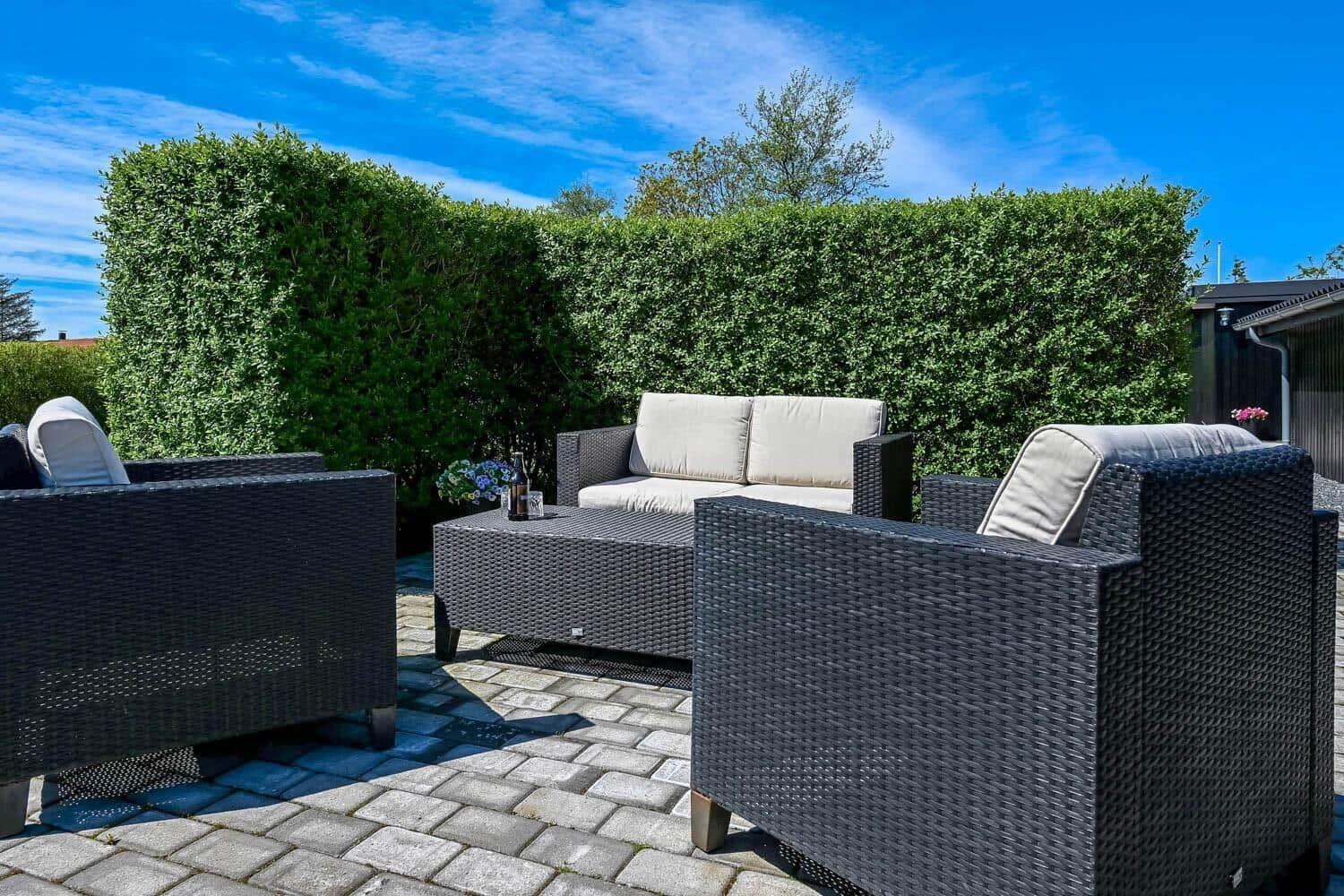 Terrasse mit Gartenmöbeln, Tisch und Beerenhecke unter blauem Himmel.