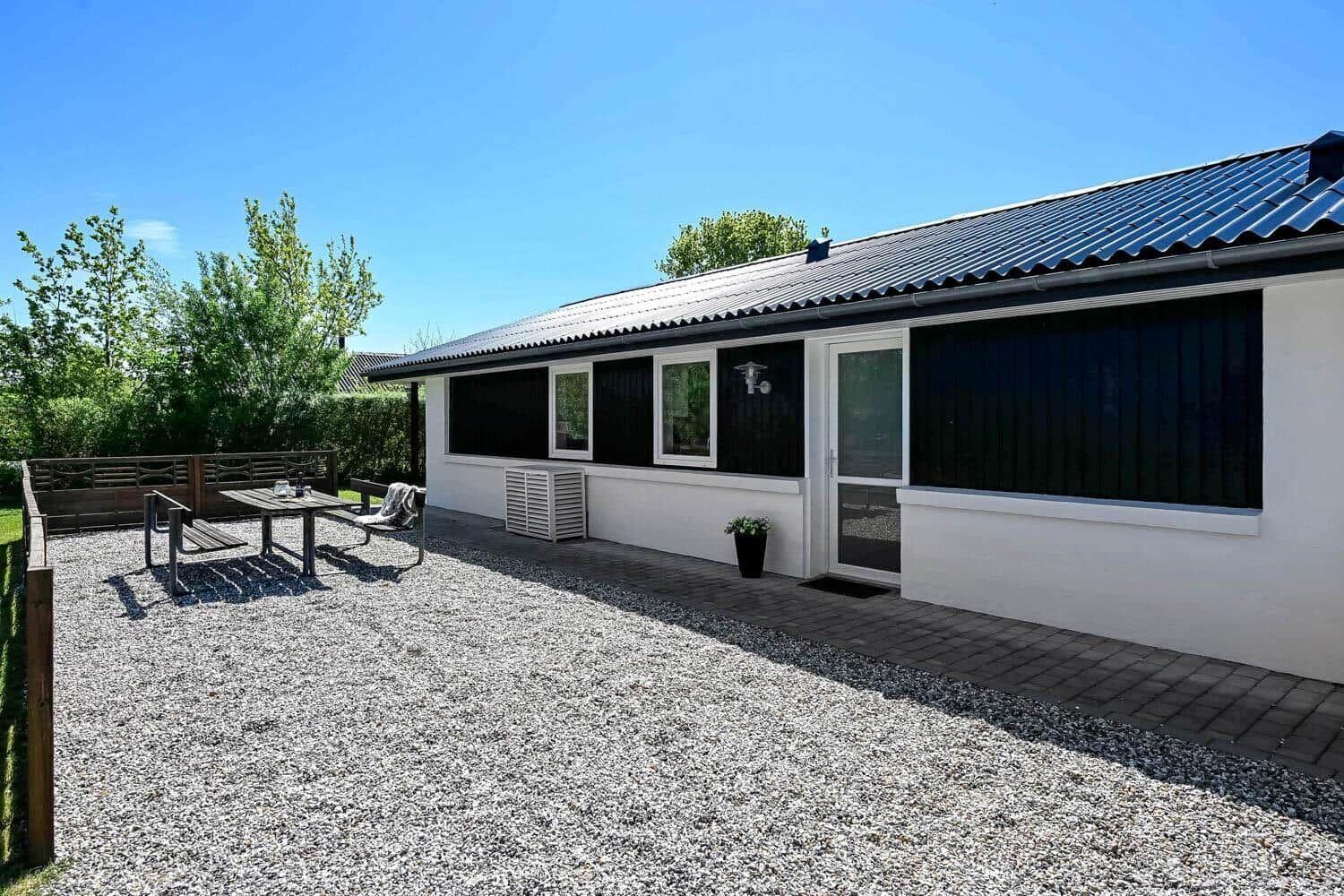 Wohnhaus mit Terrasse, Tisch und Stühlen. Außenbereich mit Kies und Pflanzen.