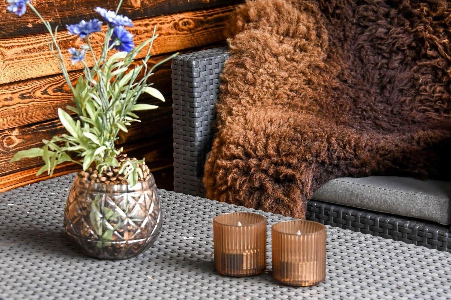 Außenbereich mit Tisch, Blumen, Kerzen und Felldecke auf Sofa