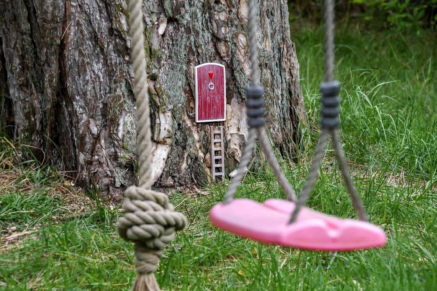 Ein kleiner roter Türchen an einem Baum mit einer pinken Schaukel im Vordergrund.