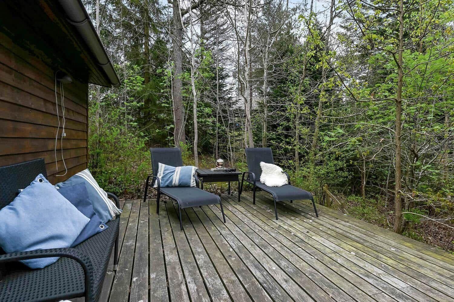 Terrasse mit Liegestühlen und Tisch im Wald. Holzdecke und Gartenmöbel.