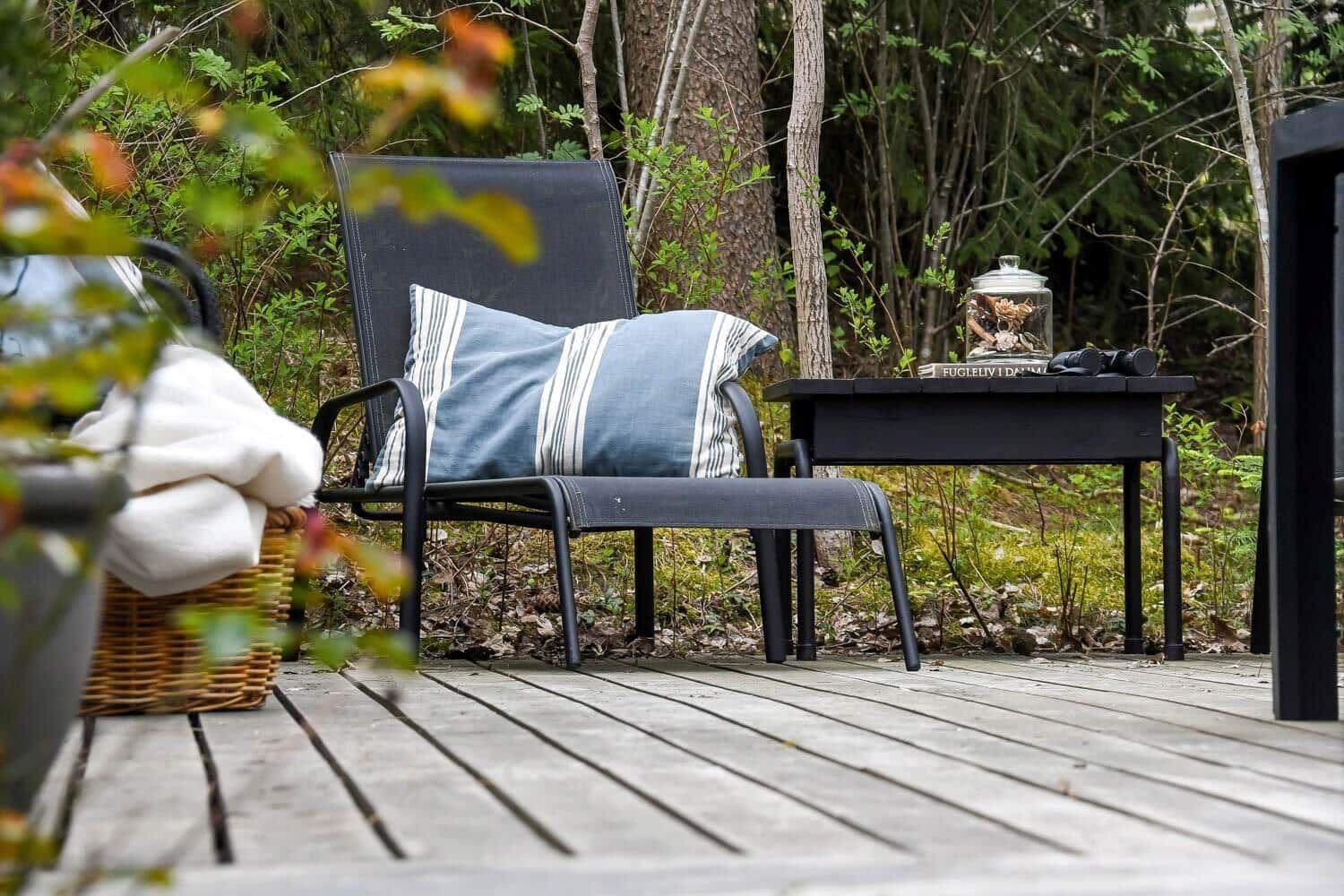Eine Außenterrasse mit Stuhl, Kissen und Tisch im Wald.