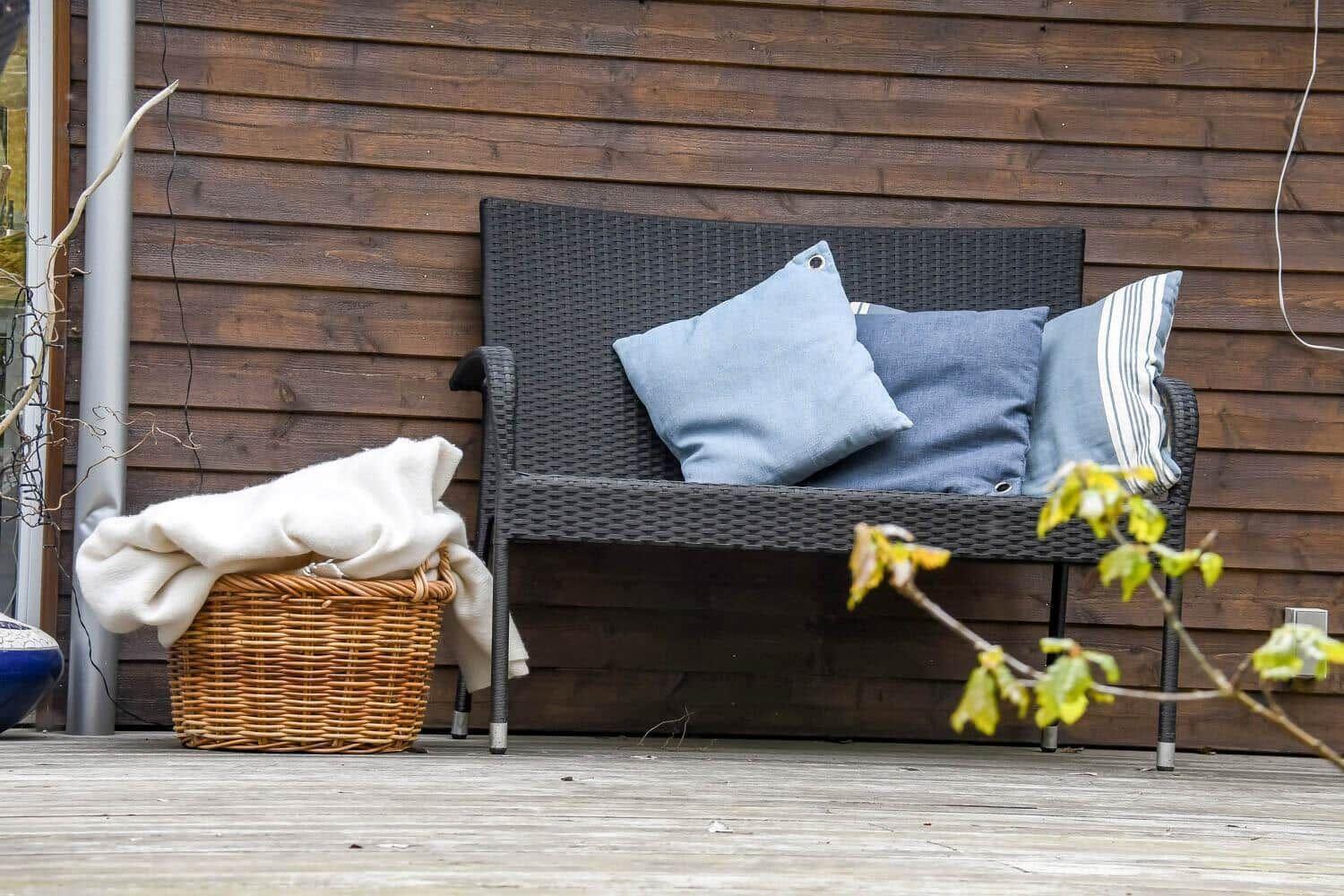 Außenbank mit Kissen und Korb mit Decke auf Holzterrasse.