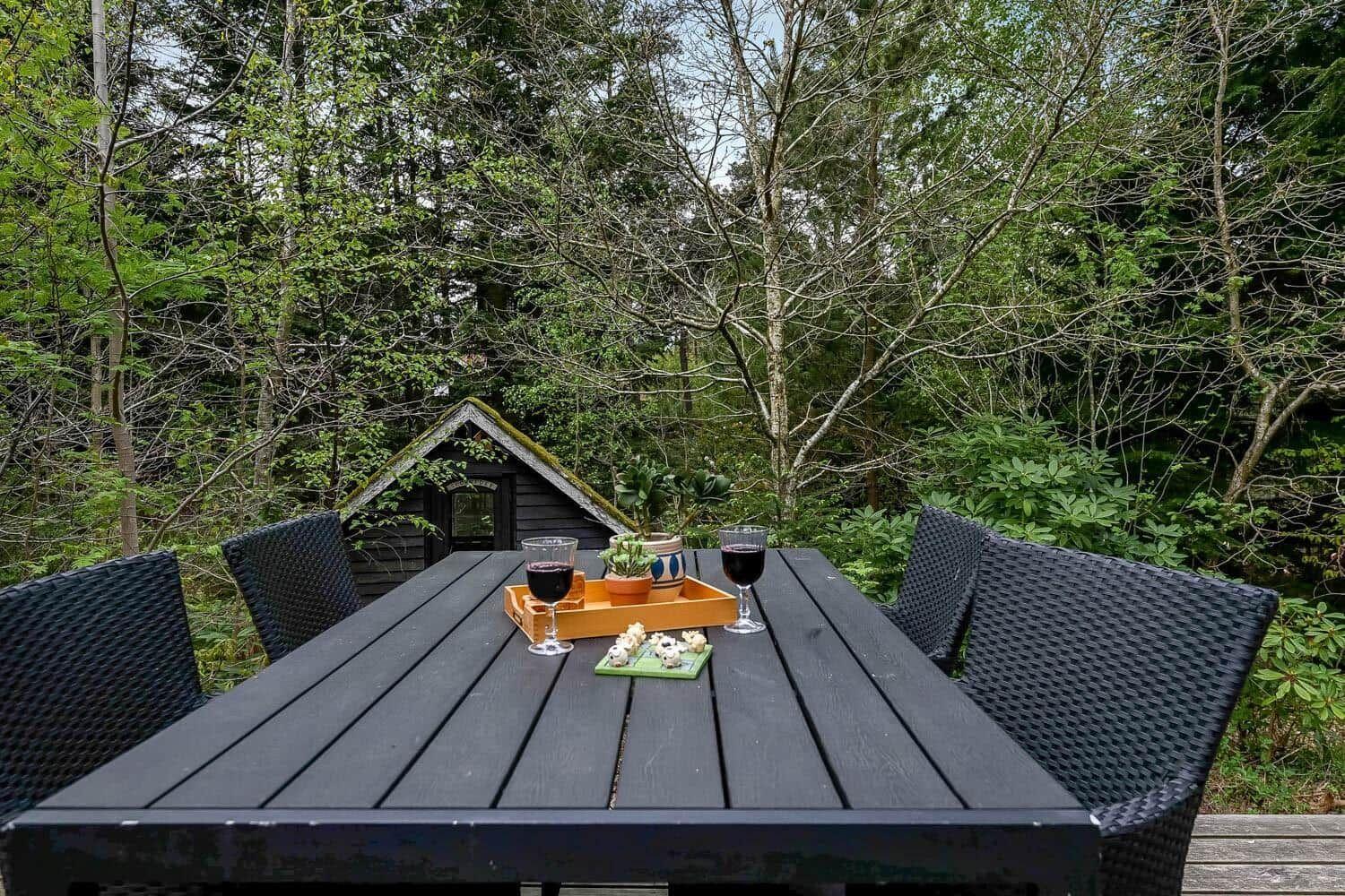 Schwarzer Holztisch mit Stühlen, zwei Weingläsern und einer Pflanze im Freien.