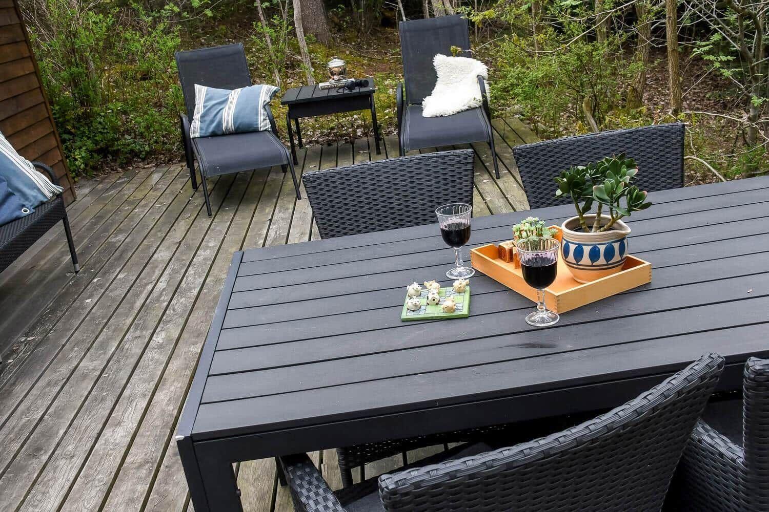 Terrasse mit Tisch, Stühlen und Pflanzen. Auf dem Tisch stehen zwei Gläser Rotwein und eine Schale mit Snacks.