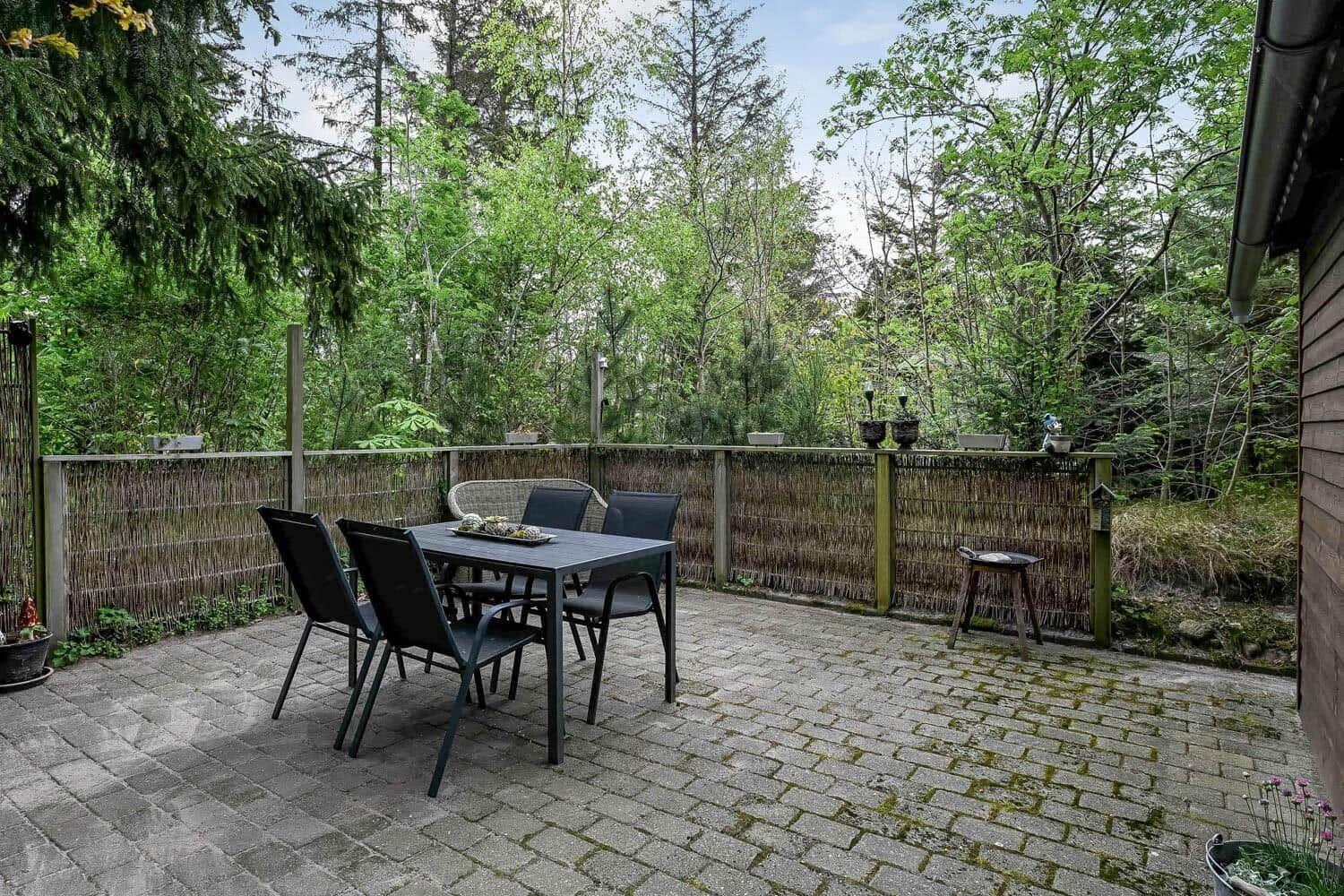 Terrasse mit Tisch und Stühlen, umgeben von Grün und Holzzaun.