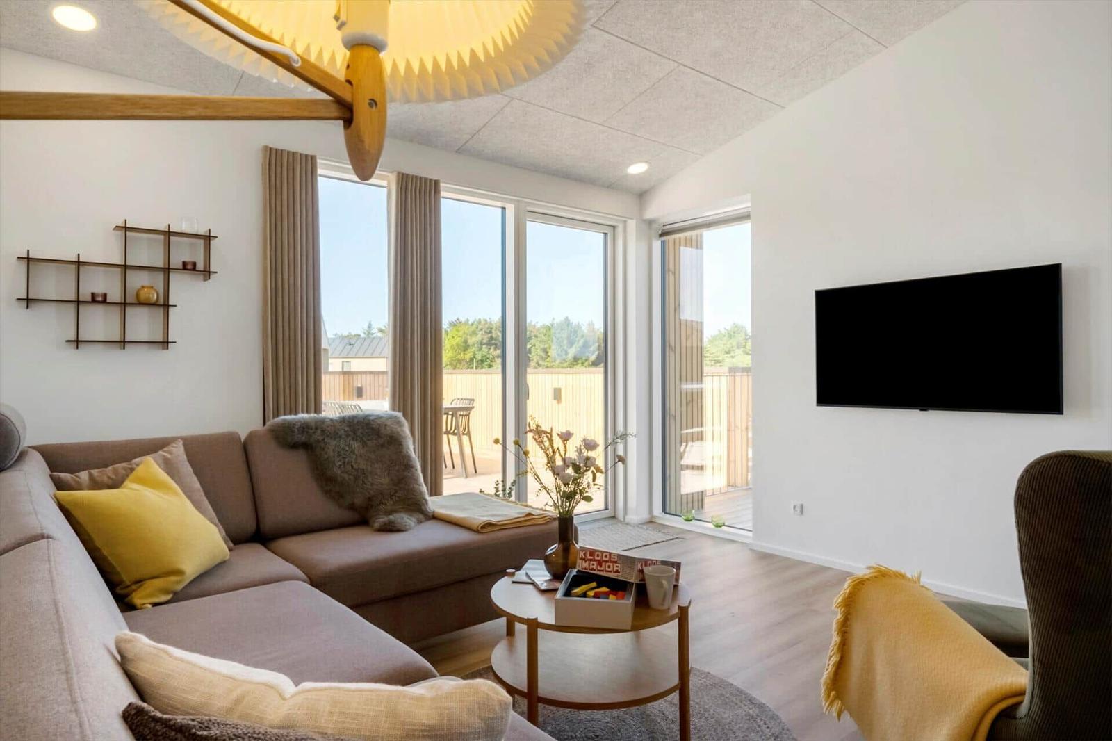Wohnzimmer mit Sofa, Fernseher und großem Fenster zur Terrasse.