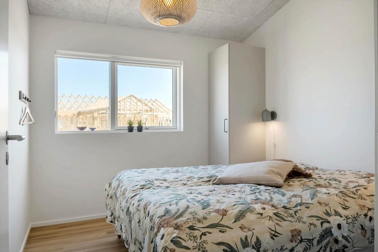 Schlafzimmer mit Bett, Fenster und Kleiderhaken an der Wand.