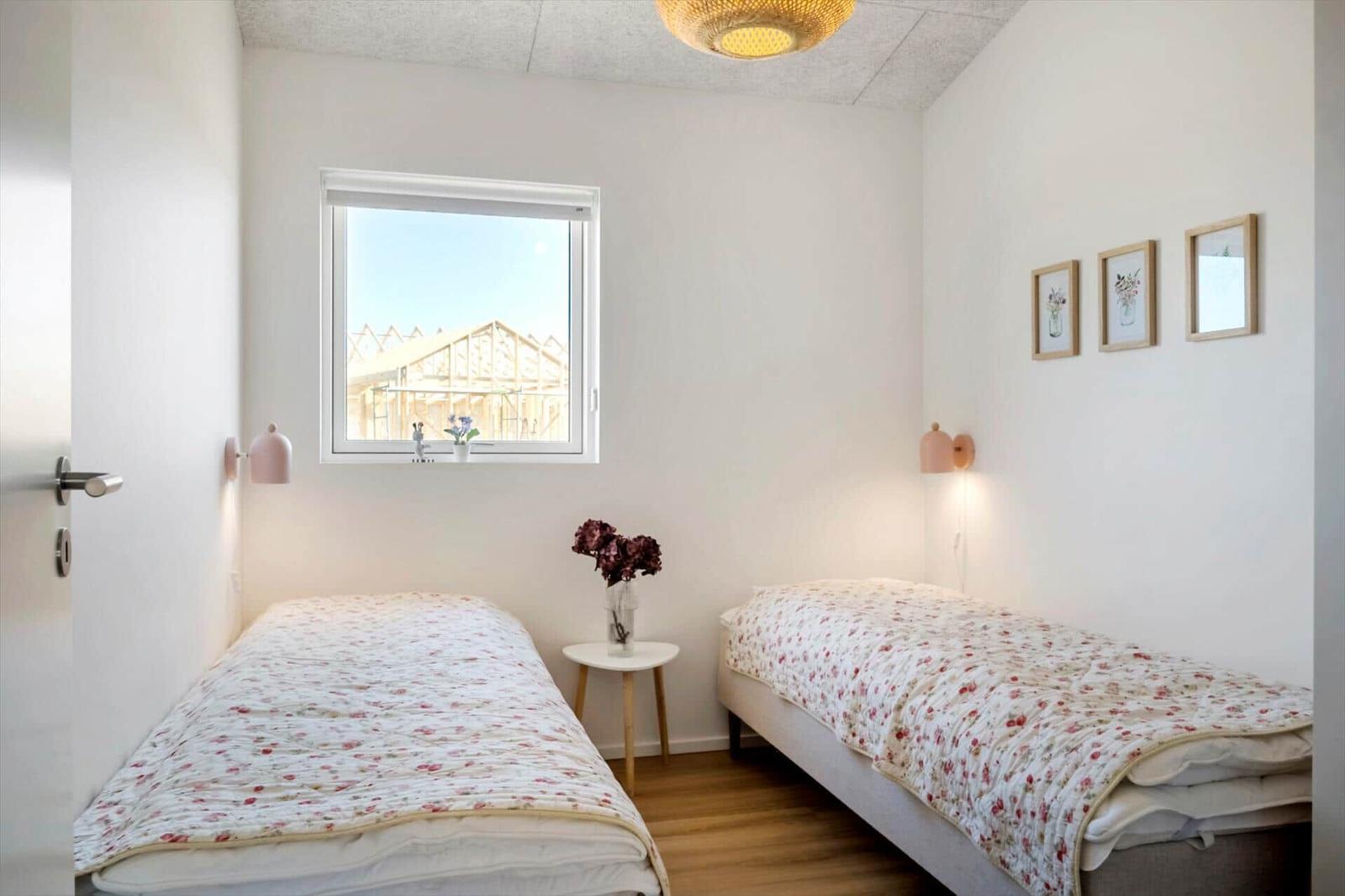 Zwei Einzelbetten mit floraler Bettwäsche, Fenster mit Blick auf Bauwerk, Wandbilder und Nachttische.