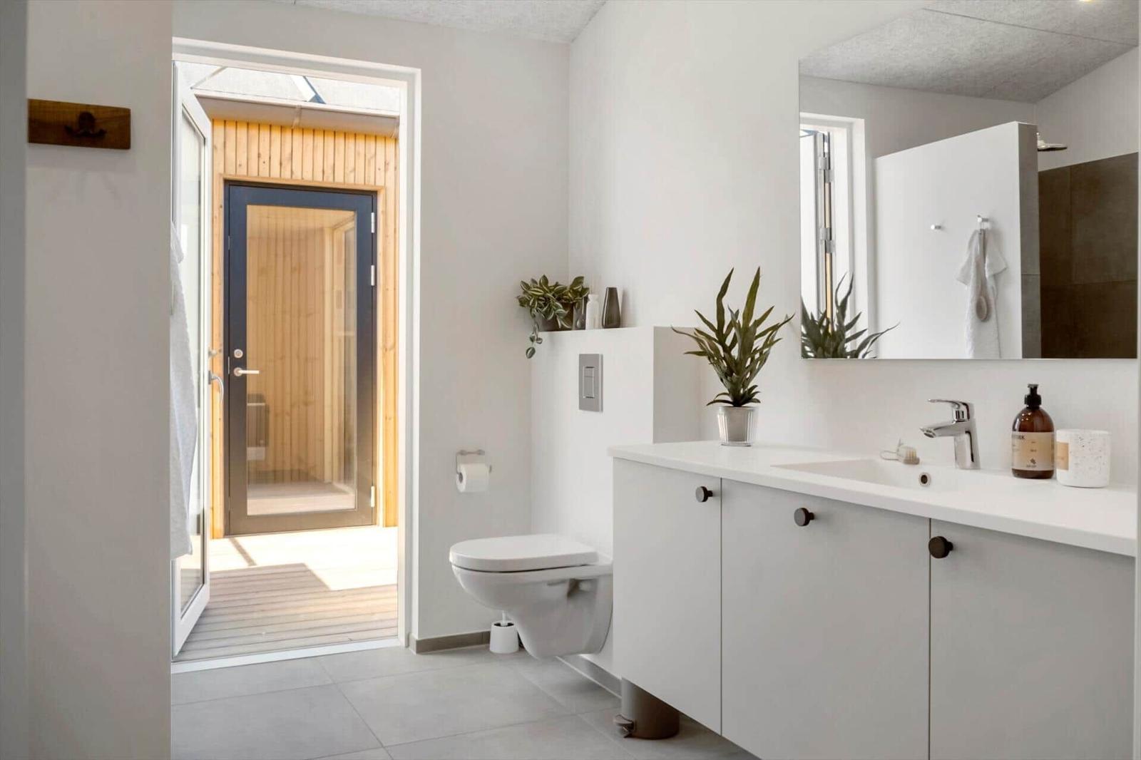 Badezimmer mit Waschbecken, Toilette und Blick auf Holzsauna.