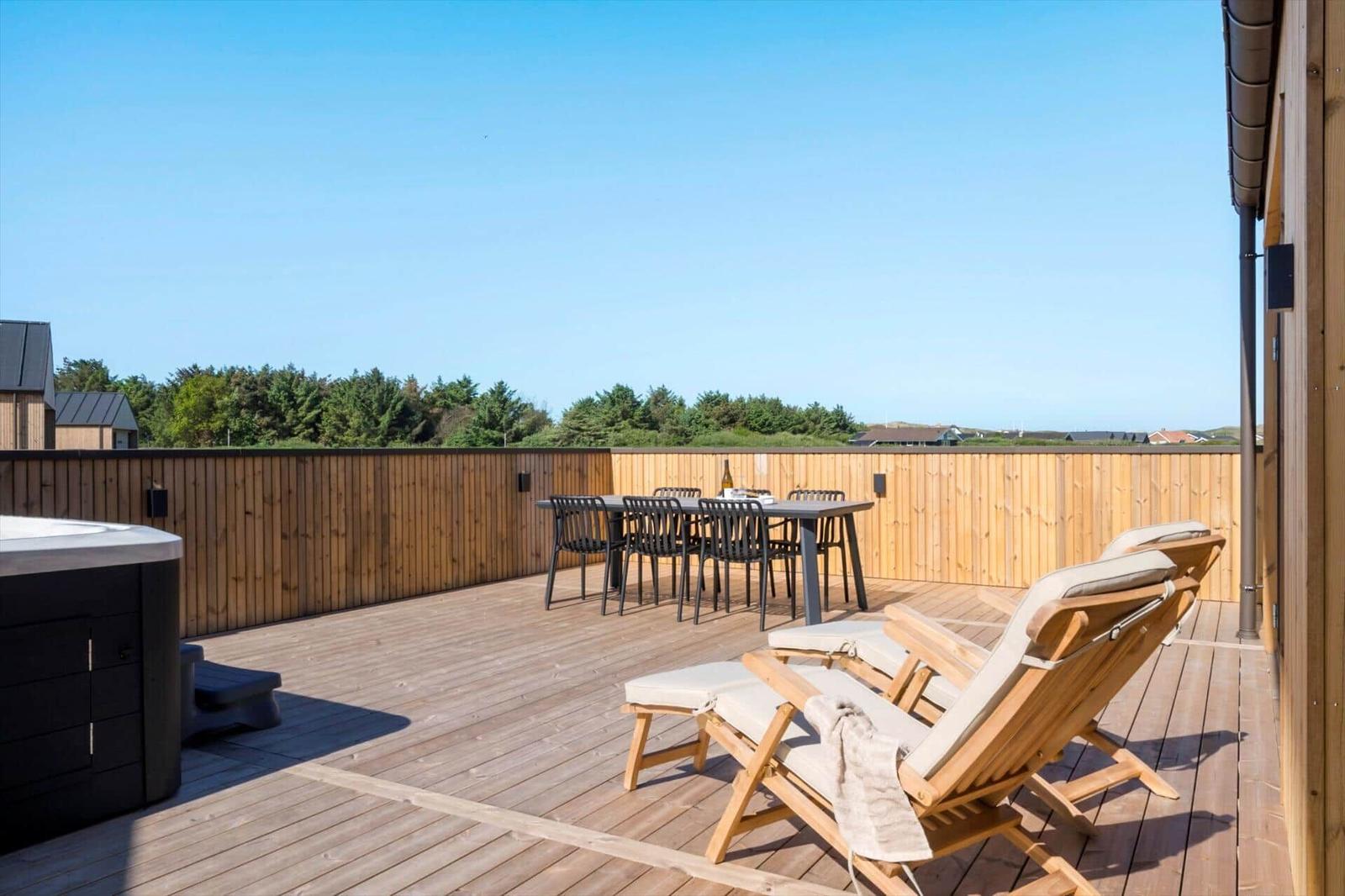 Terrasse mit Liegestühlen, Esstisch und Whirlpool. Holzgeländer und Wald im Hintergrund.