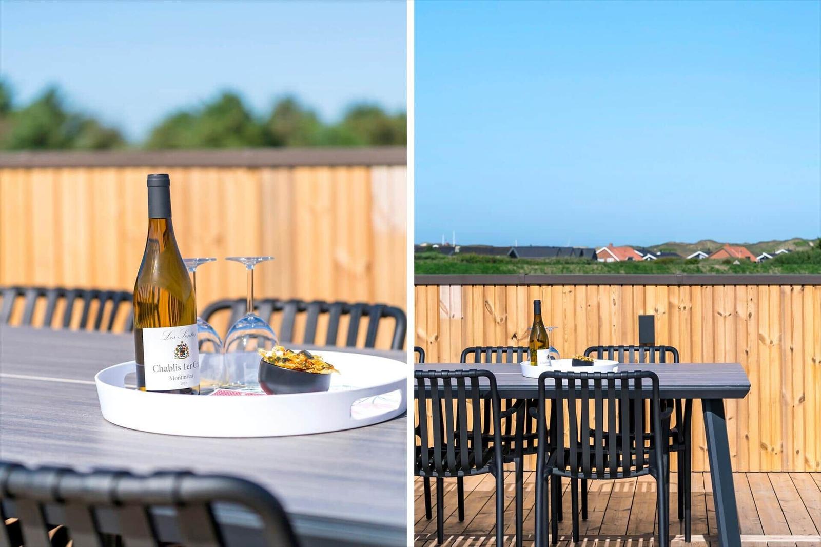 Terrasse mit Tisch, Stühlen und Weinglas. Blick auf grüne Landschaft und Häuser.