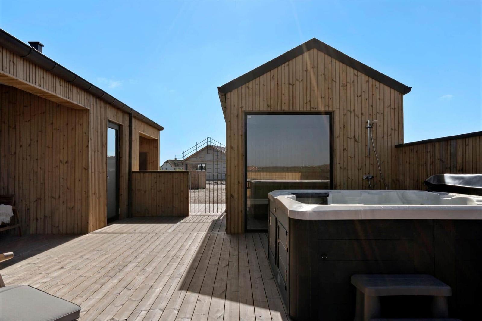 Holzterrasse mit Whirlpool und Dusche. Hintergrund: Holzgebäude und klarer Himmel.