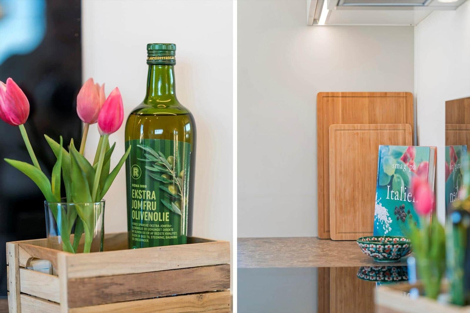 Eine Flasche Olivenöl und Tulpen in einem Holzkorb. Küchenblock und Kochbuch auf Arbeitsfläche.