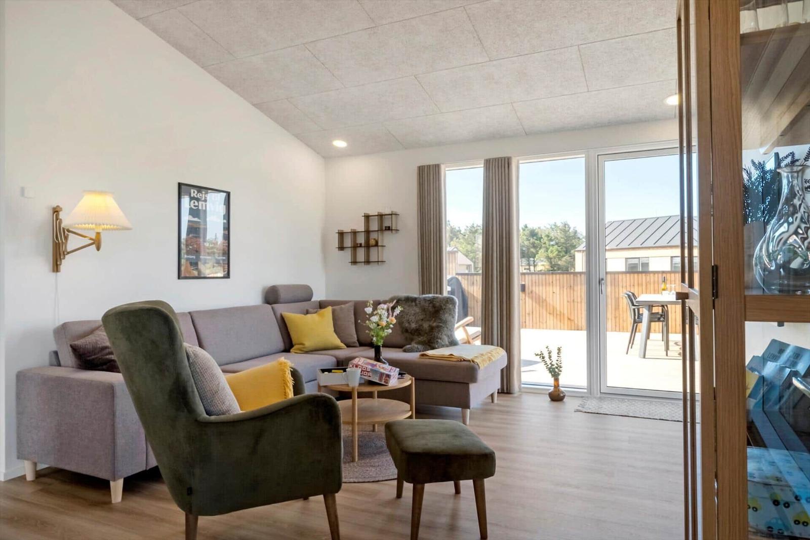 Wohnzimmer mit Sofa, Sessel und Terrasse. Durchgang zur Küche.