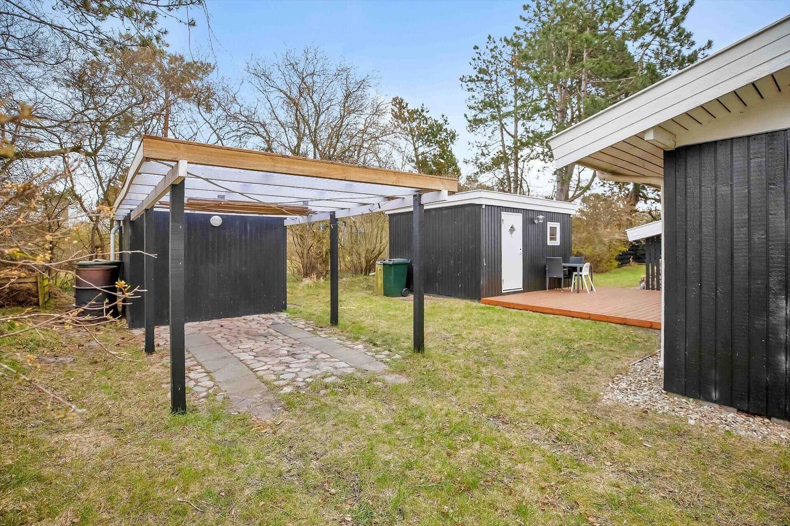 Hinterhof mit Pavillon, Terrasse und Grünfläche. Schwarze Holzstrukturen und Bäume umgeben den Außenbereich.