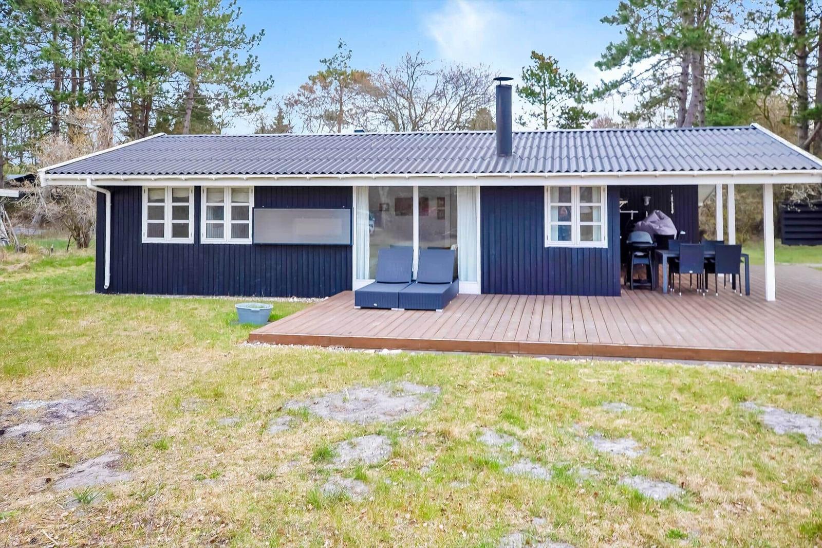 Ein dunkelblaues Haus mit Holzterrasse, Garten und Grillplatz.
