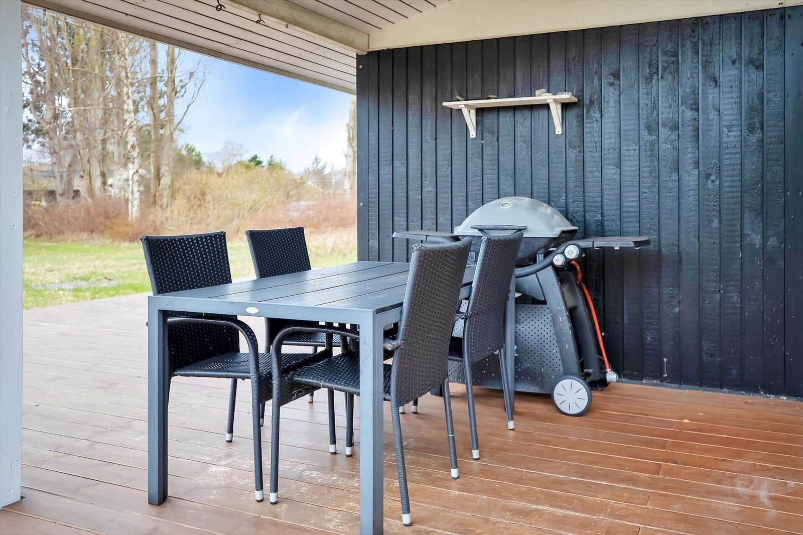 Terrasse mit Tisch, vier Stühlen und Grill an schwarzer Holzwand.