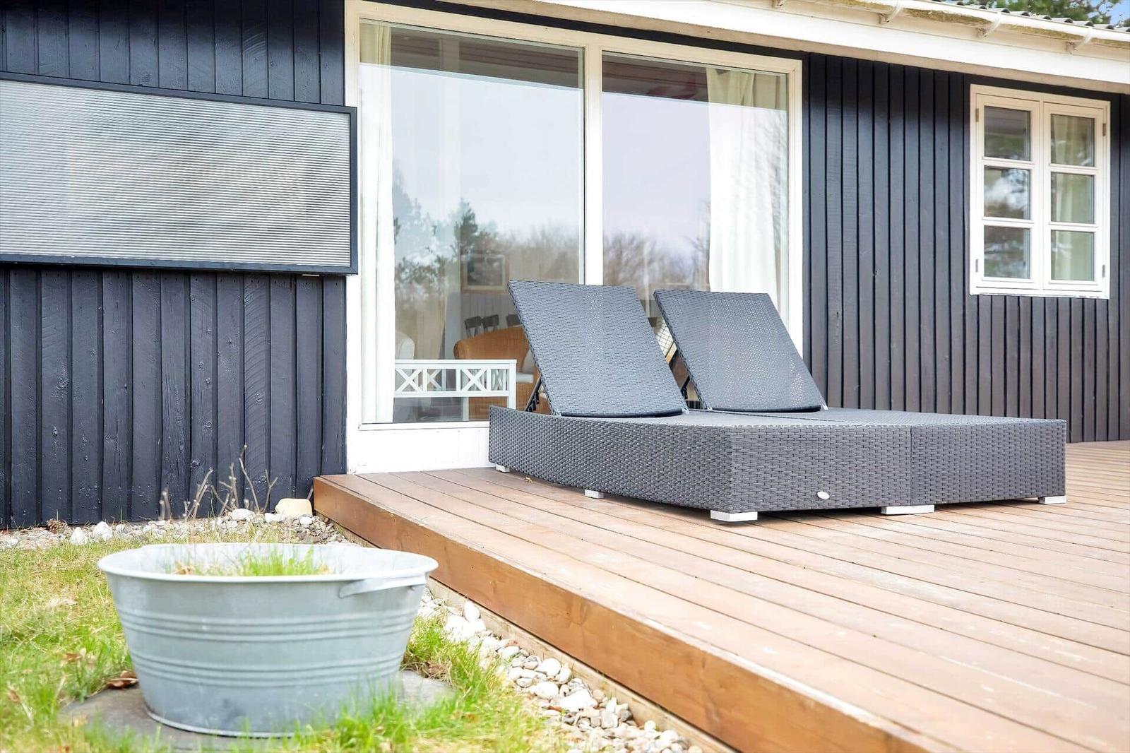 Terrasse mit Liegen vor einem Haus mit dunkler Fassade und großen Fenstern.