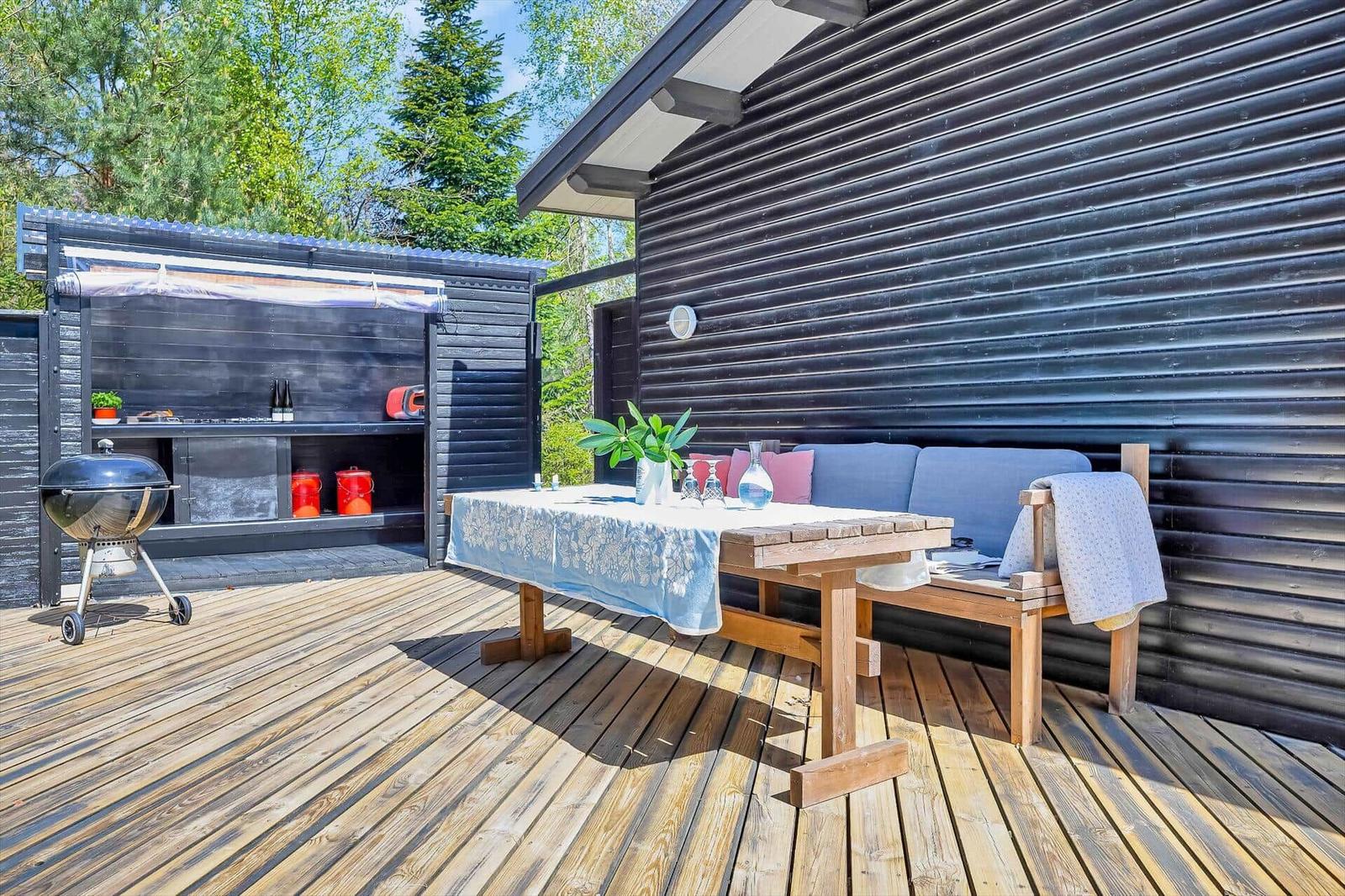 Terrasse mit Holztisch, Sitzbank und Grill. Hintergrund: schwarz lackierte Holzwand.