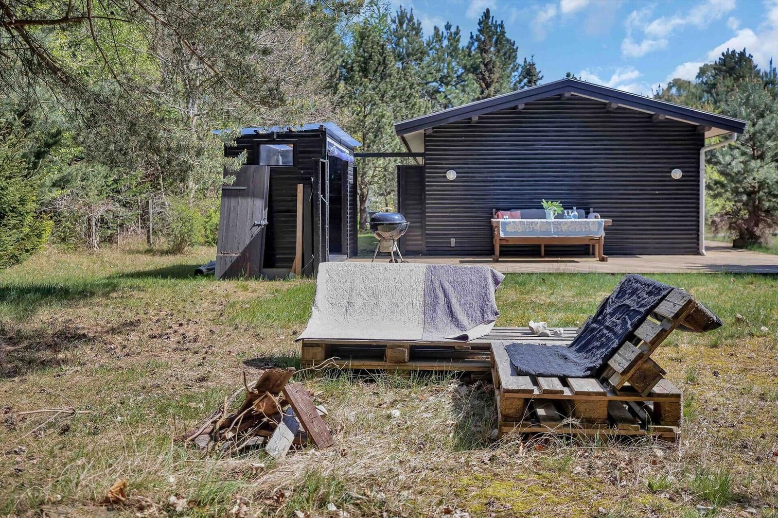 Hütte mit Terrasse, Grill und Holzliegen im Grünen.