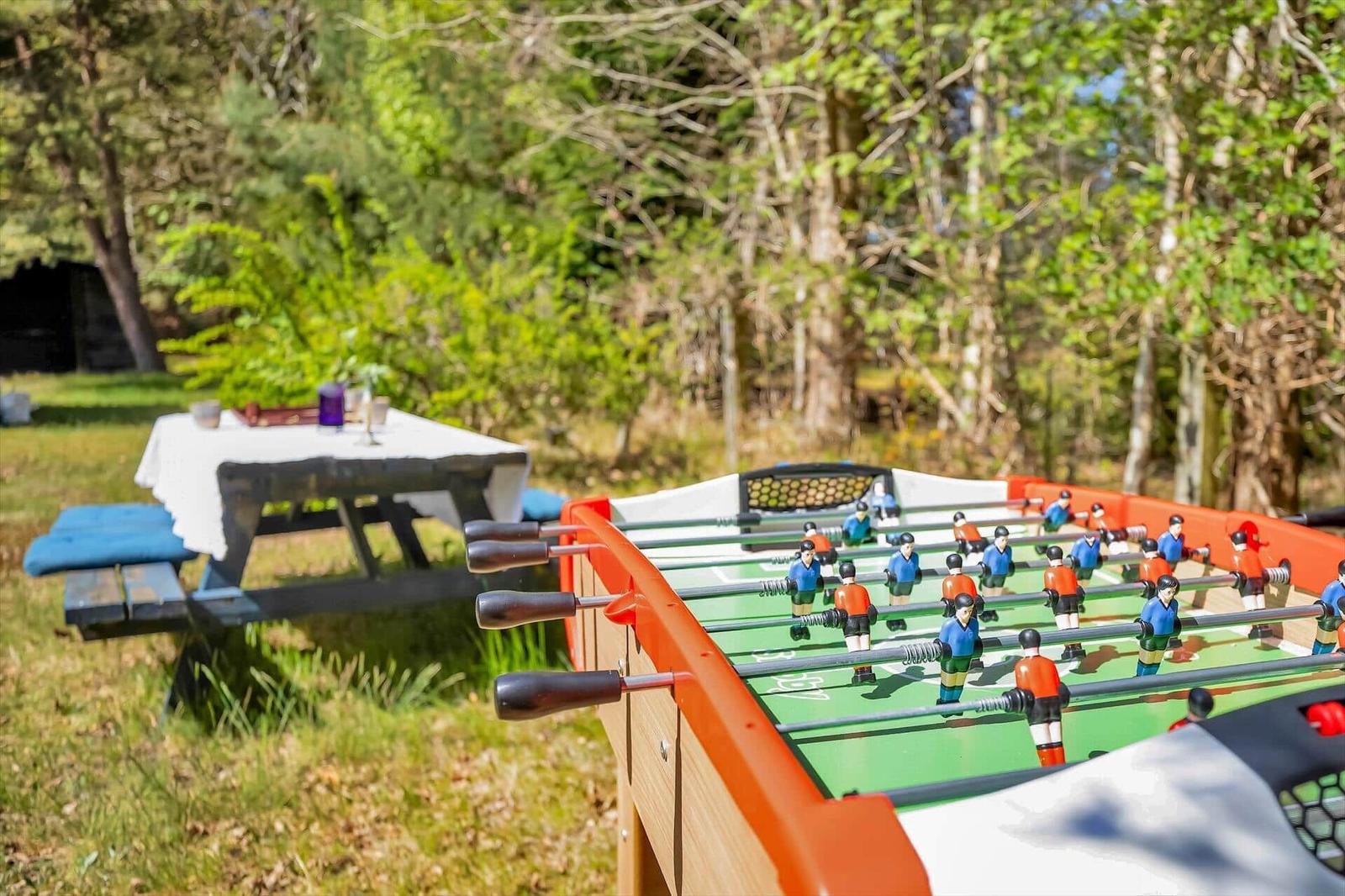 Fußballtisch im Freien, Tisch mit Tischdecke im Hintergrund, umgeben von Bäumen.