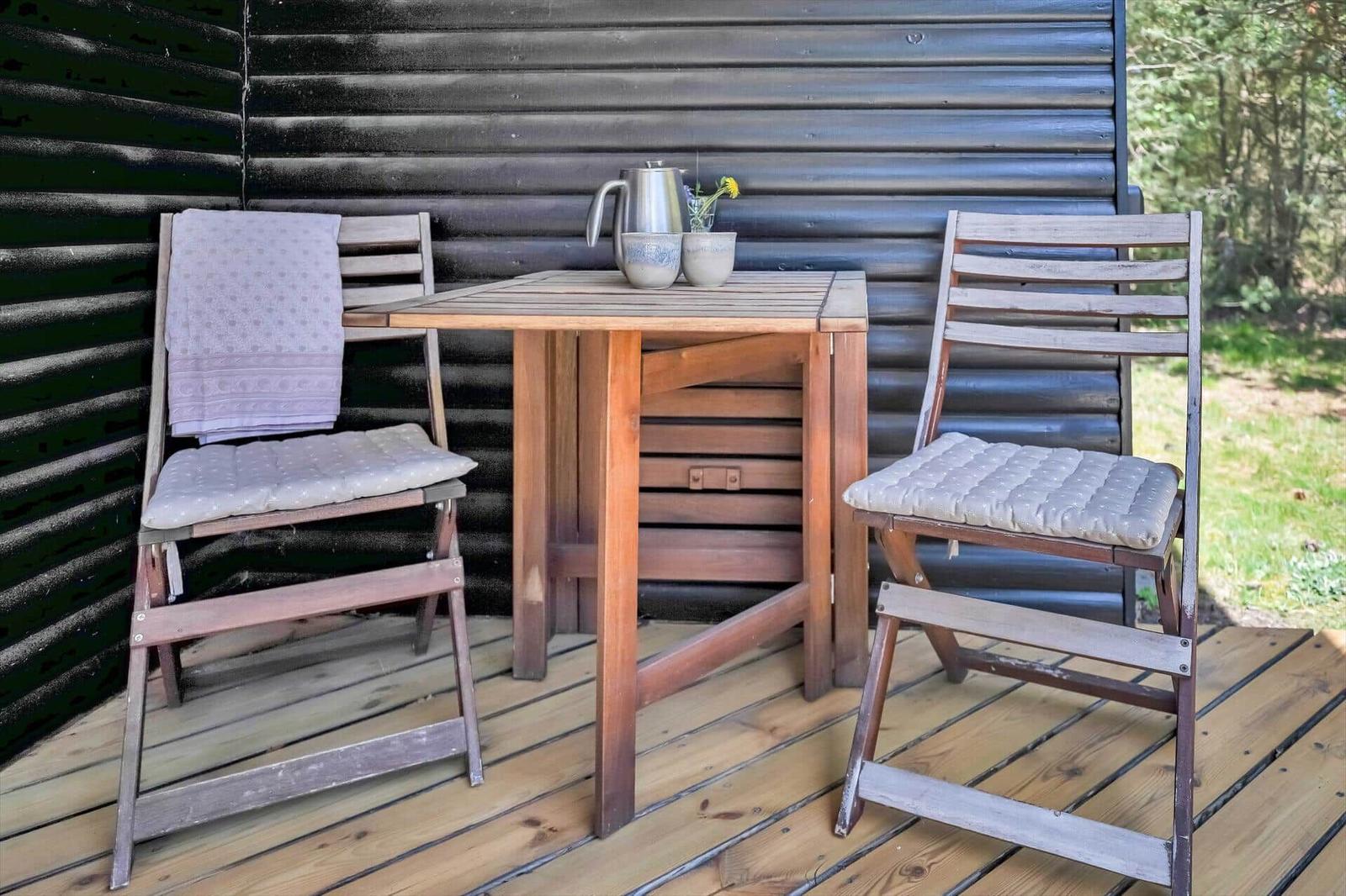 Holztisch mit zwei Stühlen auf Terrasse vor Holzwand