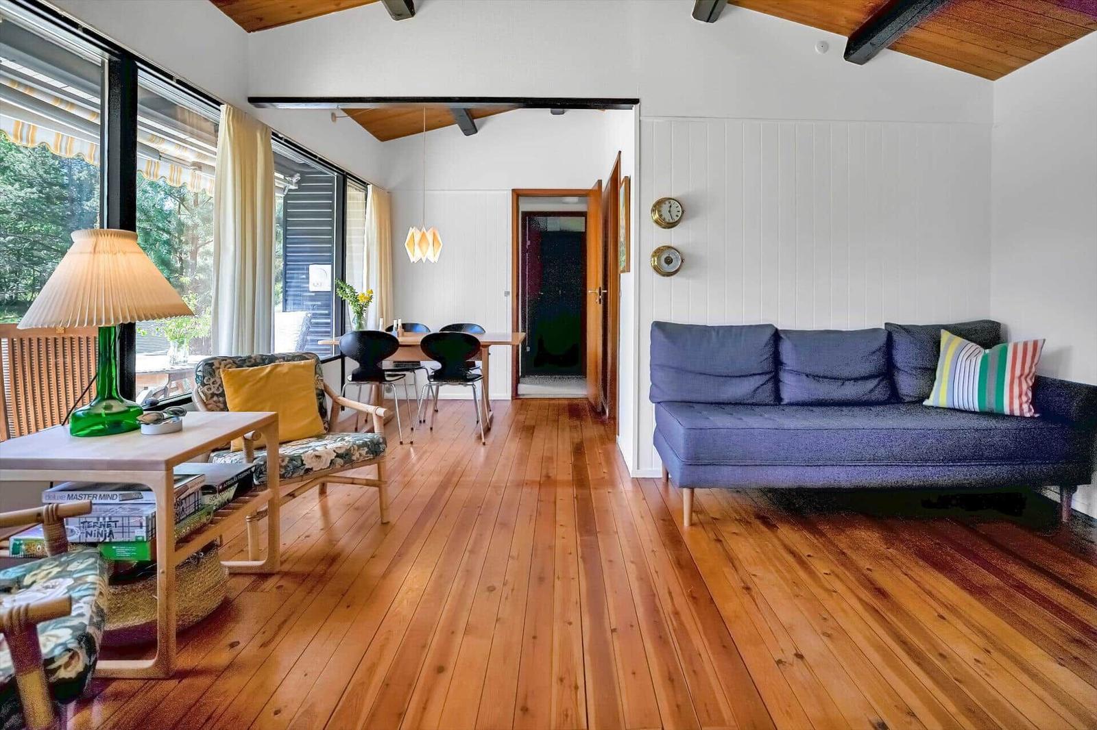 Wohnbereich mit Sofa, Tisch und Stühlen. Holzfußboden und große Fenster.
