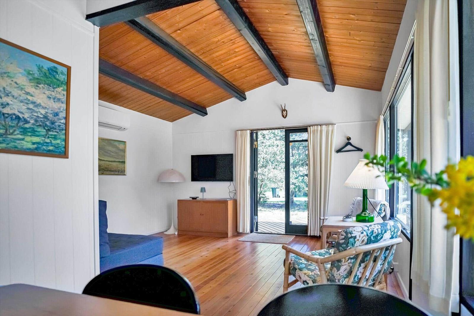 Wohnraum mit Holzboden, TV, Schlafsofa und Blick auf Terrasse.