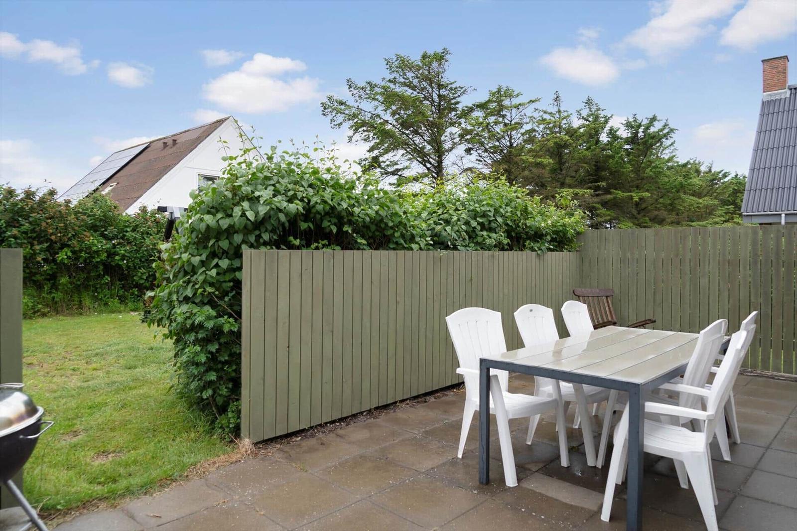 Terrace with table and chairs, surrounded by fence and greenery.