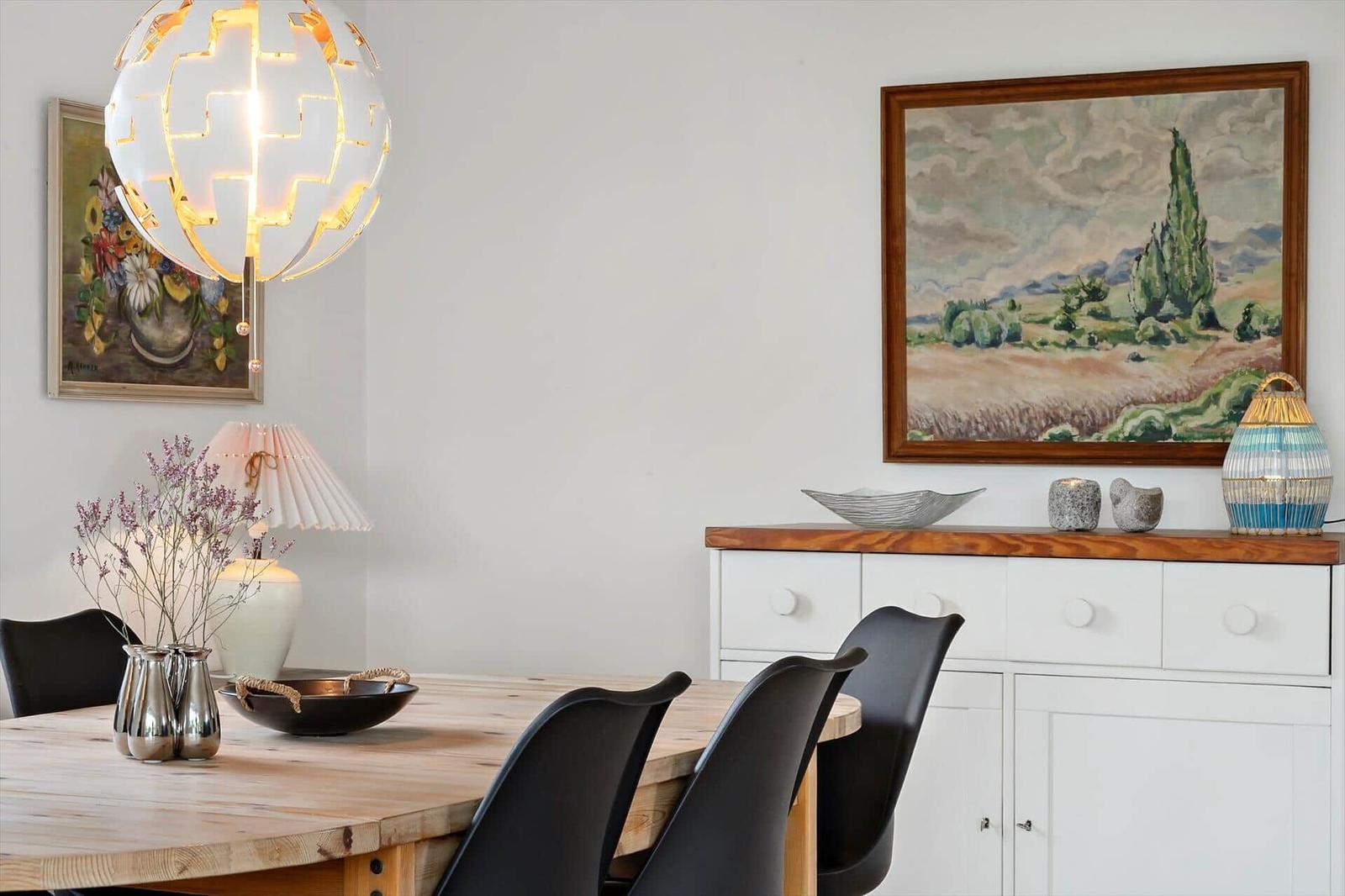 Dining room with wooden table, black chairs, and wall paintings.