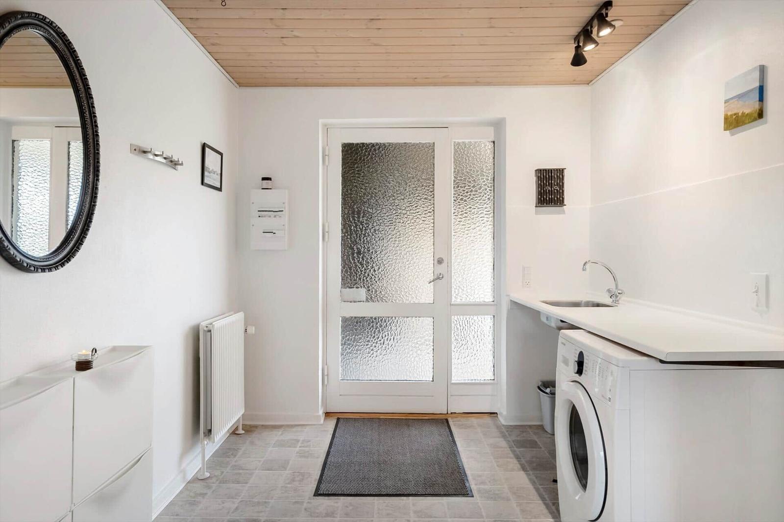 Entrance area with washing machine, sink, and decorative mirror on the wall.