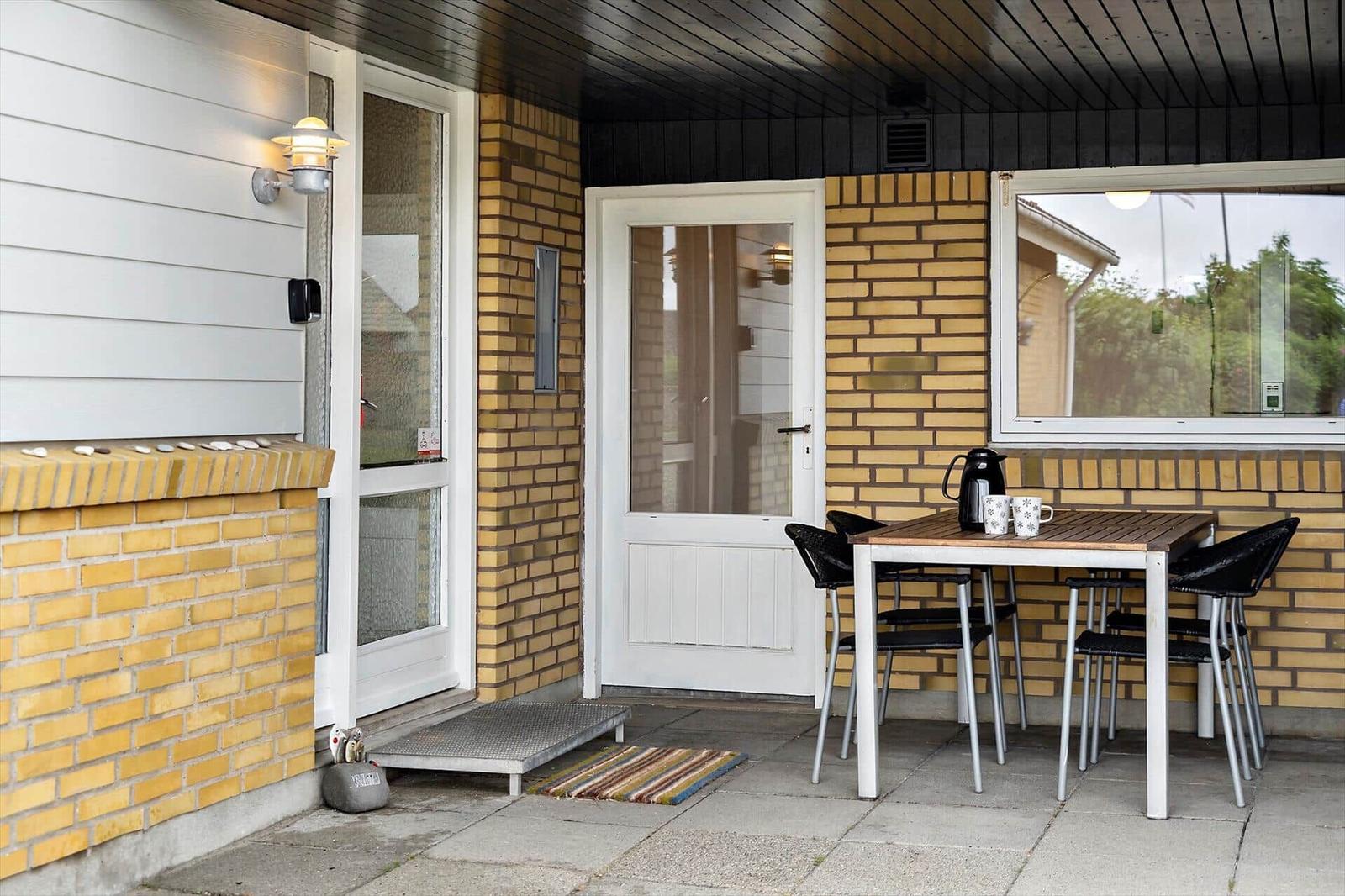 Patio with table, chairs, and coffee mugs. Yellow brick wall and white door.