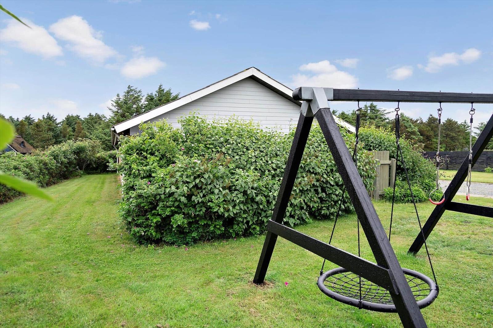 Swing in the garden in front of a house with hedge and grass