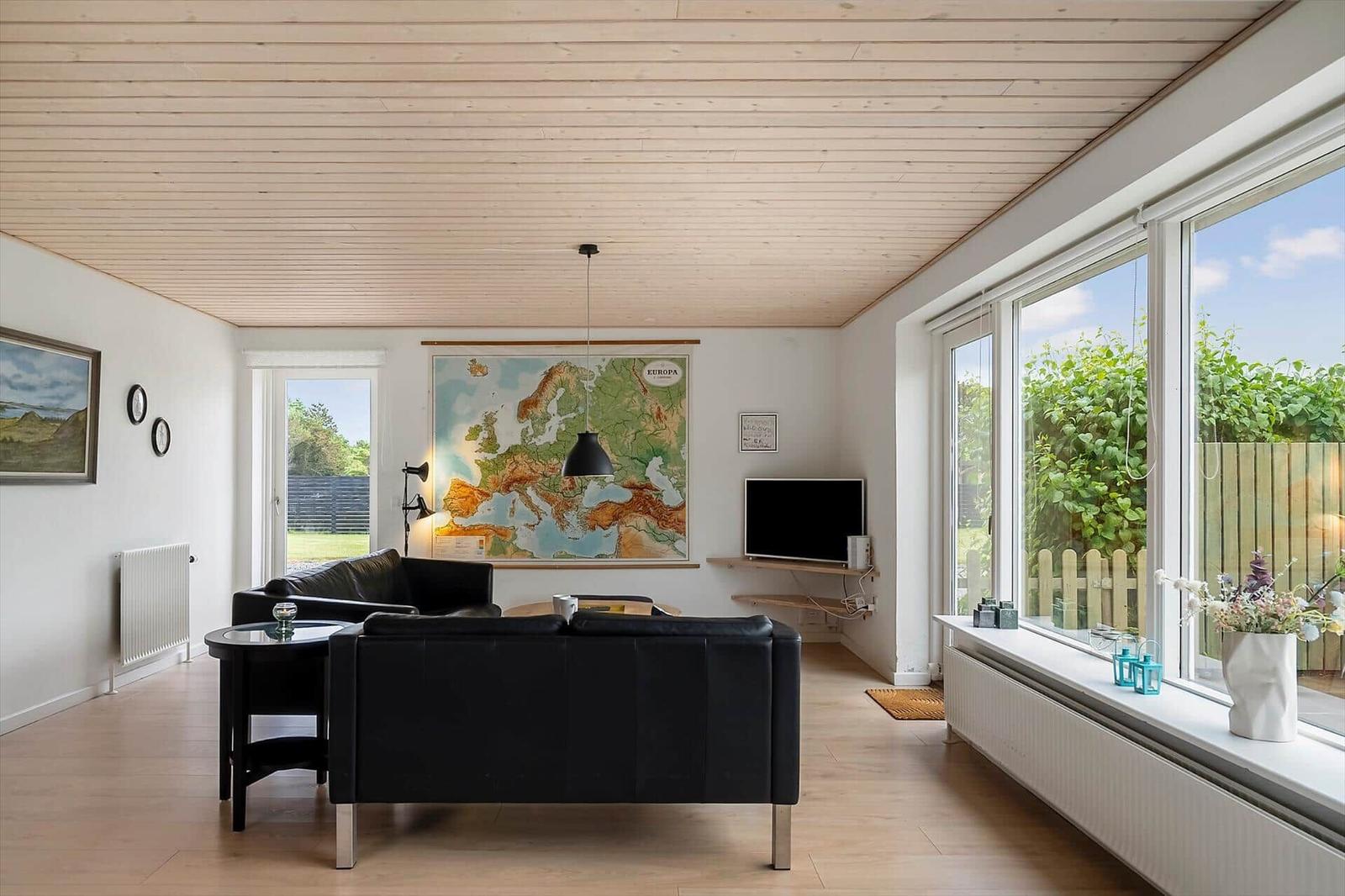 Living room with black sofa, Europe map on wall, and large window to outside.