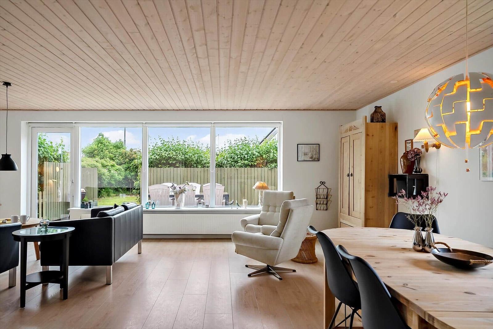 Living and dining area with wooden floor, large windows, and dining table with chairs.