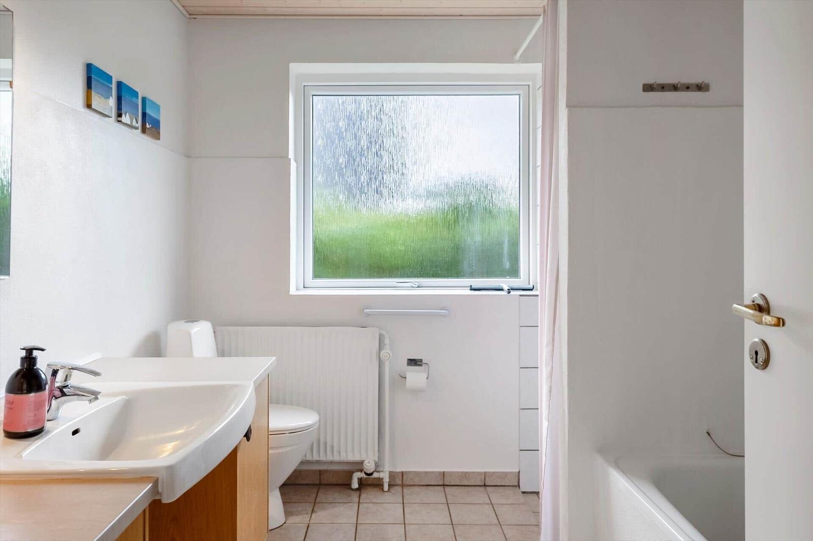 Bathroom with shower, toilet, and sink. Window with green view.