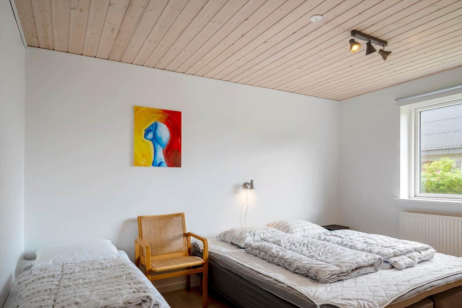 Room with two beds, wooden ceiling, wall art, and window with view of green.