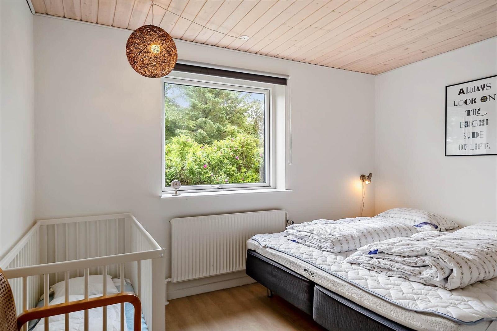 Bedroom with crib, bed, and window view of greenery.