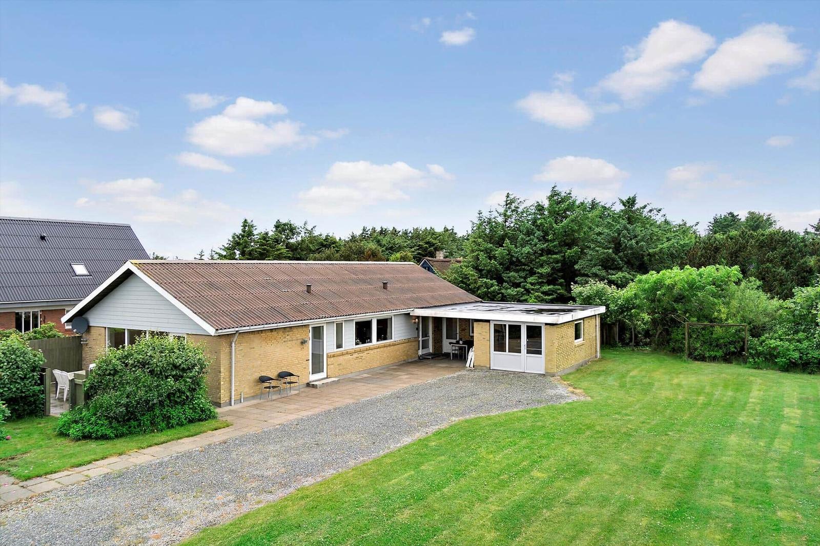 A house with garden, terrace, and barbecue area under blue sky.