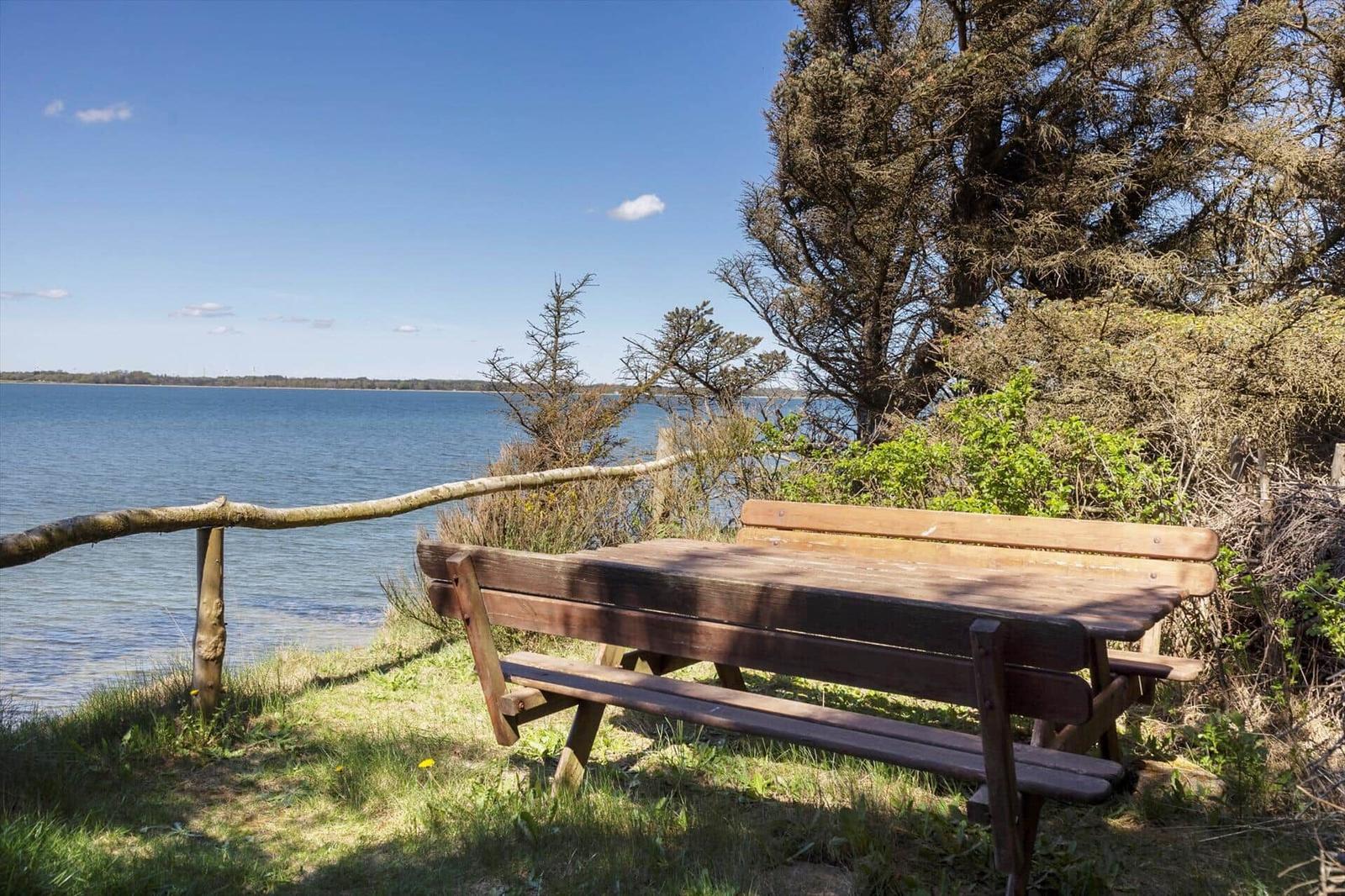 Wooden bench by water with view of lake and trees.