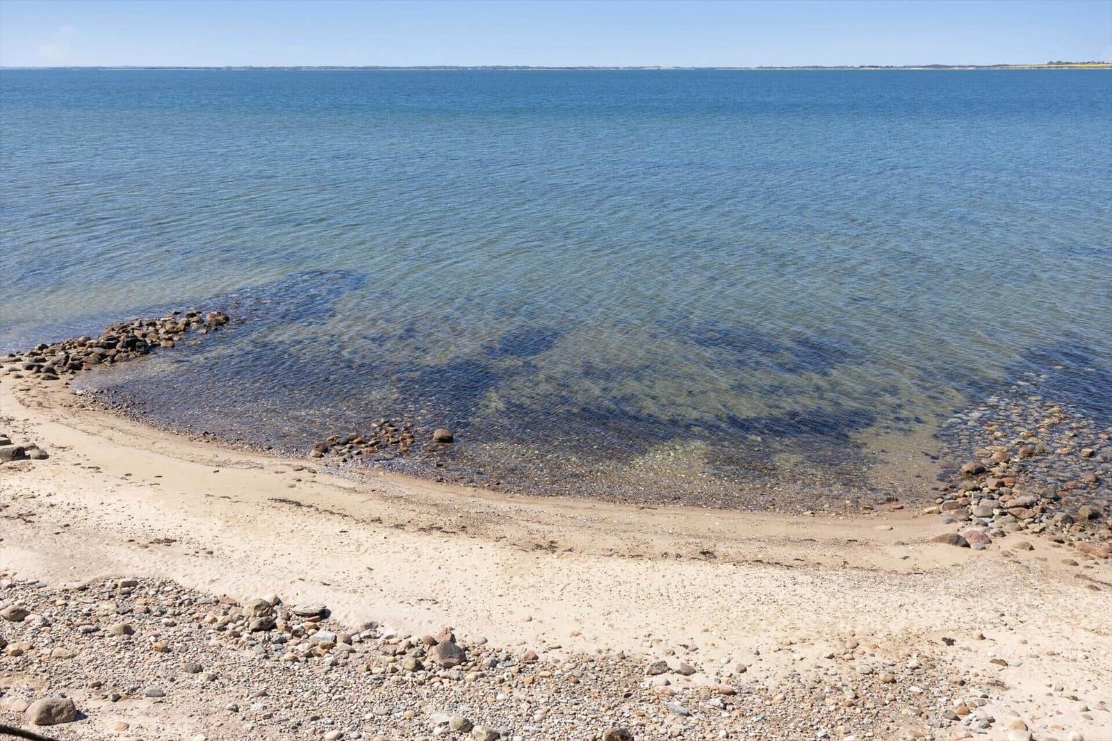 Beach with gravel and sand, clear water, horizon in the distance.