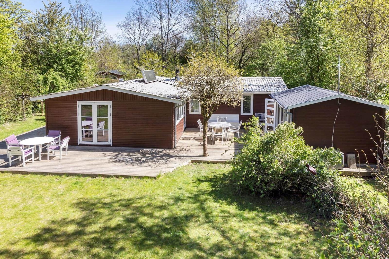 Wooden house with terrace and garden. Outdoor tables with chairs. Surrounded by trees.