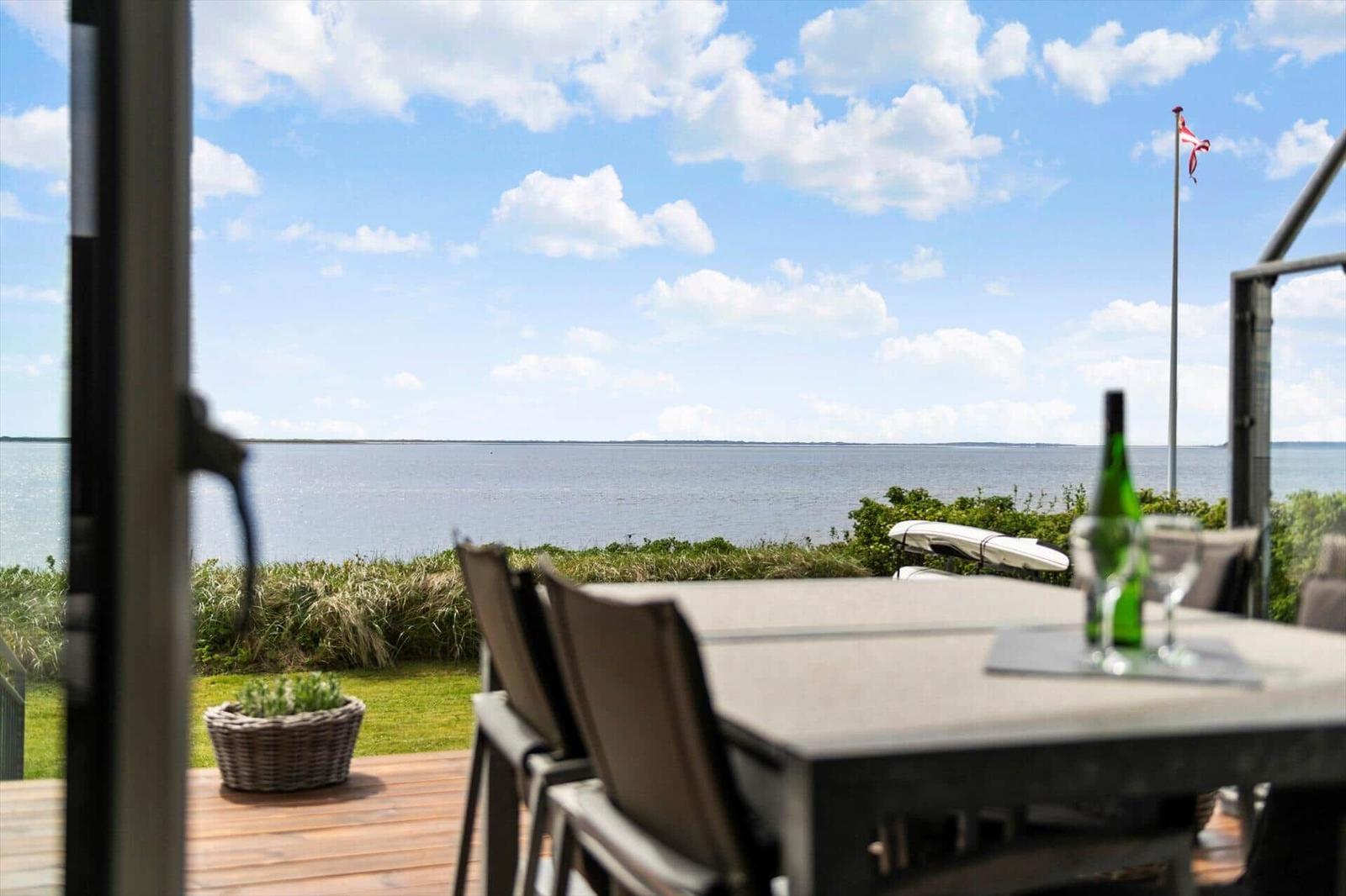 Terrasse mit Tisch und Stühlen bietet Blick auf Wasser und Himmel.