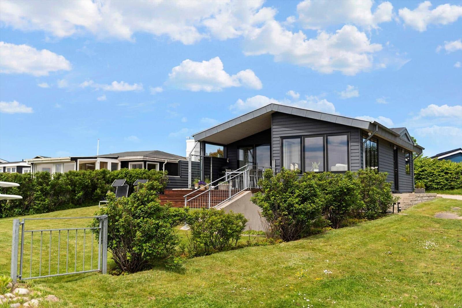 Modernes Haus mit Balkon, Grünfläche und Himmel. Eingangstreppe und Gartenzaun sichtbar.